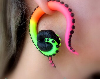 May include: A vibrant, colorful ear gauge in the shape of an octopus tentacle. The gauge features a gradient of neon colors, transitioning from green to orange to pink. The tentacle has black suction cups and a black and green head.