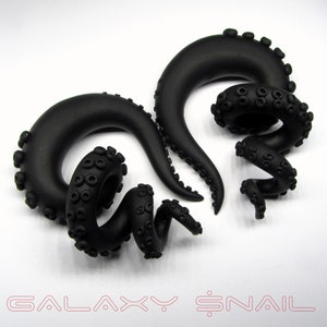 May include: A pair of black octopus-shaped ear gauges. The gauges are made of a smooth, matte black material and have a detailed octopus design. The gauges are a popular choice for body jewelry and are often worn in the earlobe or helix.