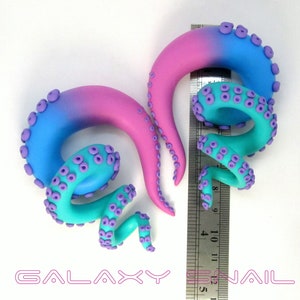 May include: A pair of handmade galaxy gradient octopus ear gauges with purple tentacles. The gauges are approximately 1 inch in diameter and are shown next to a ruler.