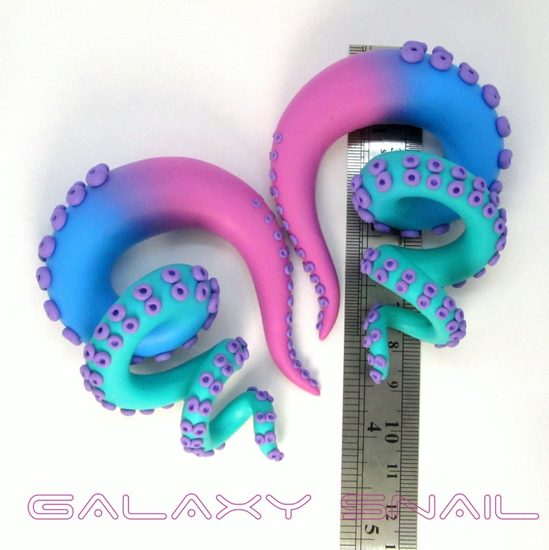May include: A pair of handmade galaxy gradient octopus ear gauges with purple tentacles. The gauges are approximately 1 inch in diameter and are shown next to a ruler.