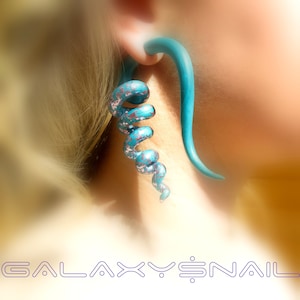 May include: A teal blue spiral ear gauge with a silver glitter finish. The gauge is worn in a person's ear.