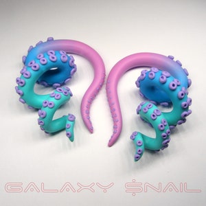 May include: A pair of galaxy-themed ear gauges with a pink and blue ombre design. The gauges are shaped like an octopus tentacle with purple accents.
