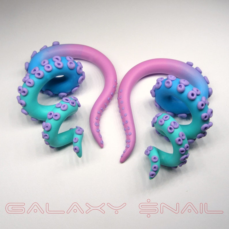 May include: A pair of galaxy-themed ear gauges with a pink and blue ombre design. The gauges are shaped like an octopus tentacle with purple accents.