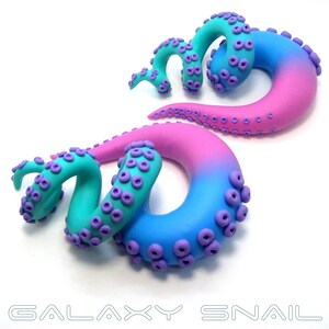 May include: A pair of galaxy-themed octopus ear gauges. The gauges are made of polymer clay and feature a gradient of pink and blue colors. The octopus tentacles are curled and have purple suction cups.