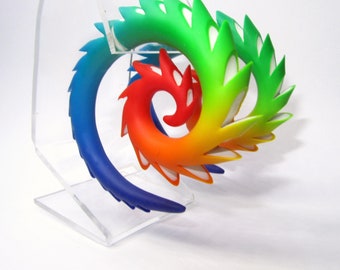 May include: A rainbow colored spiral shaped ear cuff with a layered design. The ear cuff is made of a flexible material and has a white accent.