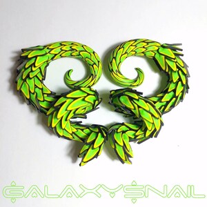 May include: A pair of green and black spiral ear gauges with a scaly design. The gauges are made of polymer clay and have a bright green and yellow color scheme.