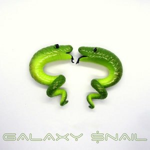 Może przedstawiać: Dwa zielone kolczyki w kształcie węża, które patrzą na siebie. Kolczyki są wykonane z polimerowej gliny i mają błyszczące wykończenie.