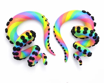 May include: Two rainbow-colored, tentacle-shaped ear gauges with black suction cup details. The gauges are in a spiral shape, with a gradient of colors including pink, yellow, green, and blue. The text "GALAXY SNAIL" is at the bottom.