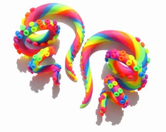 May include: Two rainbow-colored, tentacle-shaped ear gauges. The gauges are made of a smooth material and feature a vibrant gradient of colors, including red, orange, yellow, green, blue, and purple. Each tentacle has small, colorful suction cups.