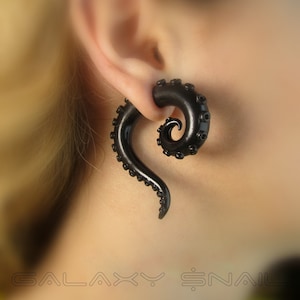 May include: Black octopus-shaped ear gauges. The gauges are made of a smooth, black material and have a spiral design. The gauges are worn in a person's ear.