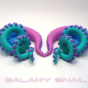 May include: A pair of handmade polymer clay ear gauges shaped like octopus tentacles. One gauge is pink and blue, the other is teal and purple. The gauges are designed to look like a galaxy.