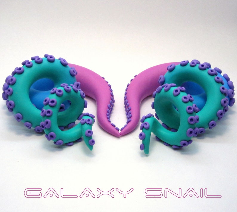 May include: A pair of handmade polymer clay ear gauges shaped like octopus tentacles. One gauge is pink and blue, the other is teal and purple. The gauges are designed to look like a galaxy.