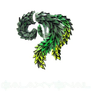 Peut inclure: Un accessoire en forme de feuille verte et jaune avec un design en spirale. L'accessoire est fait d'un matériau texturé et superposé, avec un dégradé de couleurs du vert foncé au jaune. Le texte "GALAXY SNAIL" est en bas.