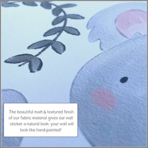 May include: Close-up of a light blue and pink fabric wall sticker with a textured finish. The sticker features a cartoon elephant with a leafy vine behind it. The text "The beautiful matt & textured finish of our fabric material gives our wall sticker a natural look- your wall will look like hand-painted!" is visible in the image.