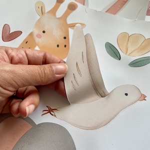 May include: A beige and brown bird with a white wing and a brown eye. The bird is a sticker and is being peeled off of a white background.