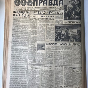 May include: A black and white newspaper with the headline "PRAVDA" in bold red letters. The newspaper is dated "Subbota 8 maya 1962 goda" and features a photo of a group of people with the caption "TRUD VO IMYA MIRA".