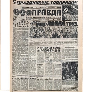May include: A black and white newspaper with the headline "С ПРАЗДНИКОМ, ТОВАРИЩИ!" (Happy Holiday, Comrades!) and the title "ПРАВДА" (Truth) in bold, red letters. The newspaper is from the Soviet Union and features a photo of a group of people celebrating May Day.