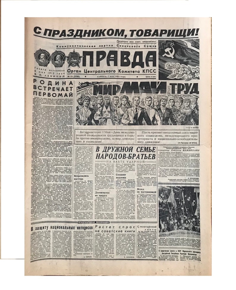 May include: A black and white newspaper with the headline "С ПРАЗДНИКОМ, ТОВАРИЩИ!" (Happy Holiday, Comrades!) and the title "ПРАВДА" (Truth) in bold, red letters. The newspaper is from the Soviet Union and features a photo of a group of people celebrating May Day.