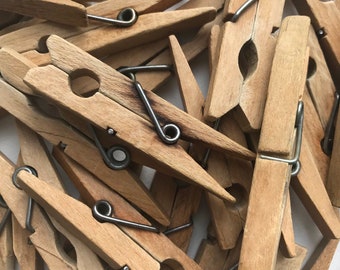 May include: A pile of wooden clothespins with metal springs. The clothespins are a light brown color and are arranged in a random pattern.