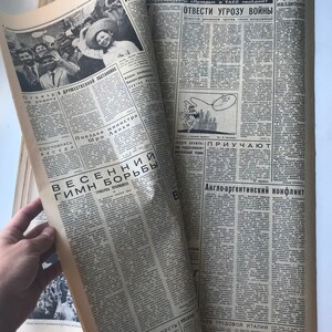 May include: A vintage newspaper with the headline "PRAVDA" and a subheading "Soviet Information" in Russian. The newspaper features a photo of a group of people, including a woman in a white dress and a hat, and a story about the "Spring Hymn of Struggle".