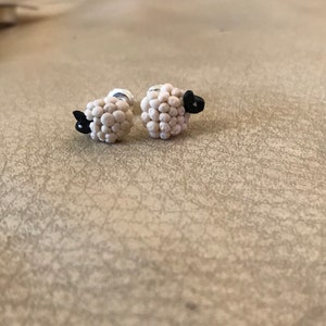 May include: A pair of silver sheep stud earrings. Each sheep is made of white beads with a black face.