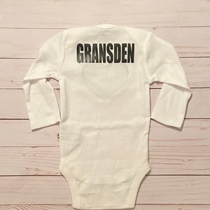 Peut inclure: Combinaison b&eacute;b&eacute; &agrave; manches longues blanche avec le mot "GRANS DEN" imprim&eacute; en noir au dos.