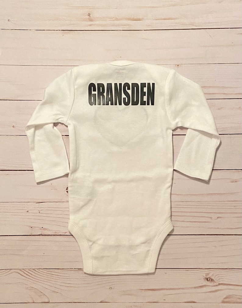 Peut inclure: Combinaison b&eacute;b&eacute; &agrave; manches longues blanche avec le mot "GRANS DEN" imprim&eacute; en noir au dos.