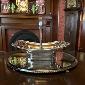 Peut inclure: Un plat de service argenté avec une poignée, posé sur un plateau miroir. Le plat a un bord festonné orné et une forme rectangulaire. La poignée est arquée et texturée. Le plateau a une bordure décorative et de petits pieds.