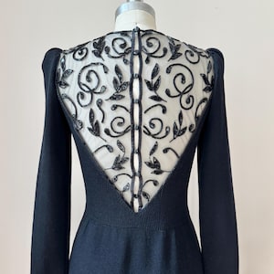 May include: A black long-sleeved dress featuring a sheer upper back panel with intricate black beadwork in a swirling leaf pattern. The back includes a vertical row of small black buttons running down the center of the sheer mesh section.