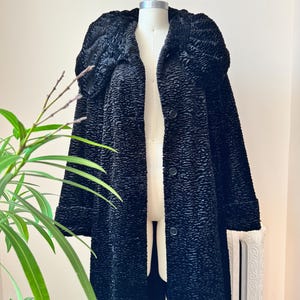 May include: A long, black textured coat with a large collar and three buttons. The coat is displayed on a mannequin. The coat's fabric has a unique, raised pattern. The coat's sleeves are long and the coat reaches the ankles.