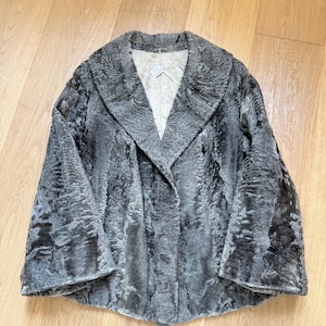 May include: A vintage grey fur coat with a wide collar and flared sleeves. The coat has a textured appearance and a light-coloured lining. The coat is buttonless and appears to be in good condition.