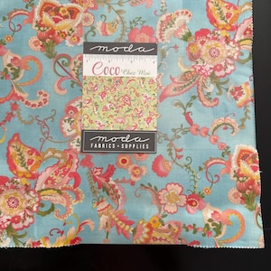 May include: A square fabric sample featuring a light turquoise background with a floral paisley pattern in pink, orange, and yellow. A smaller swatch with a green background and a similar floral design is attached. The text "moda Coco Chez Moi FABRICS + SUPPLIES" is visible.