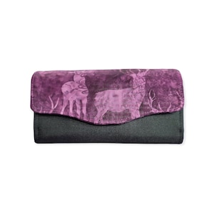 Peut inclure: Un portefeuille noir avec un rabat orné d'un motif de cerf violet et blanc. Le portefeuille est de forme rectangulaire et possède une fermeture à bouton-pression. Le motif de cerf est une silhouette.