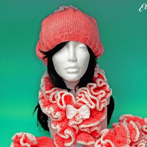 Puede incluir: Un conjunto de gorro, bufanda y guantes de punto de ganchillo rosa. El gorro es de estilo beanie holgado. La bufanda es un cuello de volantes. Los guantes son sin dedos con un borde de volantes.