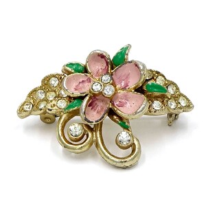 May include: A gold-tone brooch featuring a pink enamel flower with green enamel leaves and clear rhinestones.