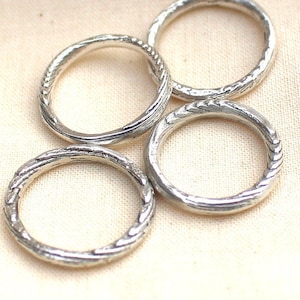 Könnte beinhalten: Vier silberne Ringe mit einem strukturierten, geflochtenen Design. Die Ringe sind übereinander gestapelt.