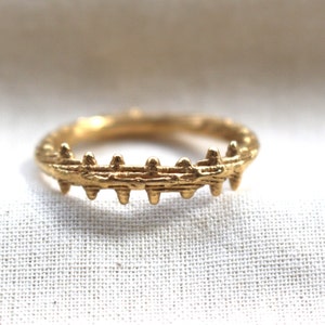 Könnte beinhalten: Ein goldener Ring mit einem strukturierten, organischen Design. Der Ring hat eine Reihe kleiner, spitzer Vorsprünge entlang der Oberkante.