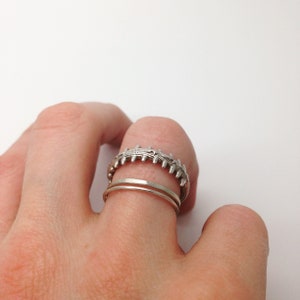 May include: Two silver rings on a finger. The top ring has a textured design, while the bottom ring is a simple band.