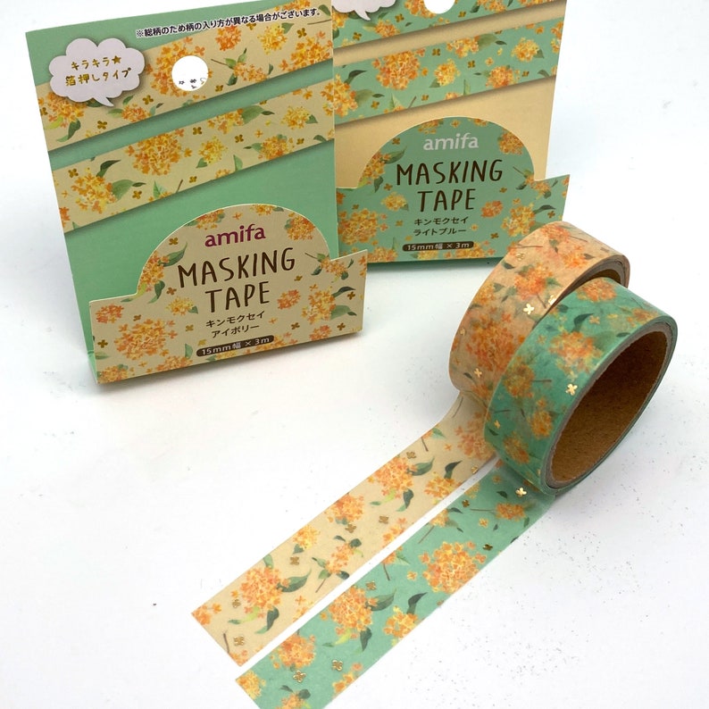 Peut inclure: Deux rouleaux de ruban adh&eacute;sif washi avec un motif floral. Le ruban mesure 15 mm de large et 3 m de long. Le ruban est emball&eacute; dans une bo&icirc;te verte et jaune avec le texte "amifa masking tape" et "キンモクセイ" (kinmokusei, qui signifie osmanthus).