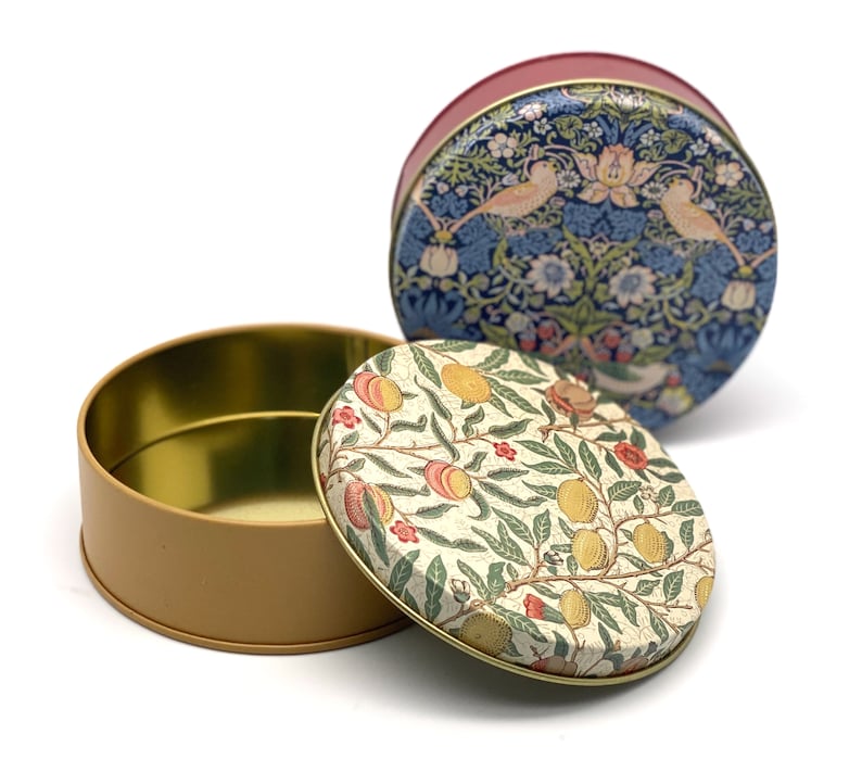 May include: Two round tin boxes with floral patterns. The top box has a blue and white floral pattern with birds. The bottom box has a cream and red floral pattern with fruit.