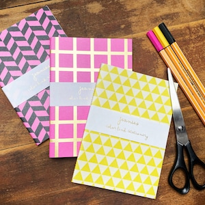 Könnte beinhalten: Drei kleine Notizbücher mit verschiedenen geometrischen Mustern. Die Notizbücher sind rosa, gelb und schwarz-weiß. Die Notizbücher tragen den Text "Jeanie's color line stationery".