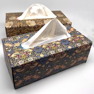 Può includere: Due scatole di fazzoletti rettangolari decorative con motivi floreali. Una scatola presenta uno sfondo blu navy con un colorato motivo floreale e di uccelli. L'altra ha uno sfondo marrone con un motivo floreale color crema. I fazzoletti bianchi sono visibili.