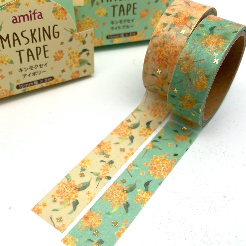 Peut inclure: Deux rouleaux de ruban adh&eacute;sif washi avec un motif floral et des paillettes dor&eacute;es. Le ruban mesure 15 mm de large et 3 m de long. Le ruban est emball&eacute; dans une bo&icirc;te avec le nom de la marque "amifa" et le texte "masking tape" en japonais et en anglais.