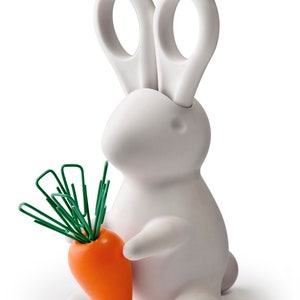 May include: A white bunny-shaped desk organizer holding an orange carrot with green paperclip 'greens'. The bunny has large ears and a smooth, matte finish. A fun and functional office supply.