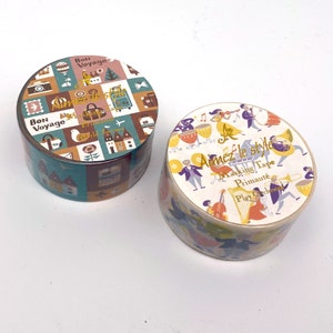 May include: Two rolls of washi tape with colourful designs. The first roll features a travel theme with images of suitcases, aeroplanes, and houses. The second roll features a musical theme with images of musicians playing instruments. Both rolls have the text "Aimez le style" on them.
