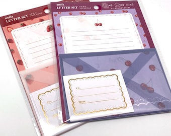 Könnte beinhalten: Zwei Sets Briefpapier mit Kirsch- und Erdbeer-Motiv. Jedes Set enthält Umschläge, Briefpapier und kleine Karten mit den Etiketten "An" und "Von". Das Kirsch-Set ist lila und das Erdbeer-Set ist rosa.