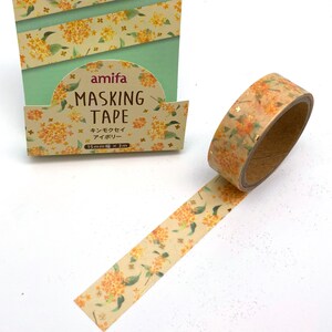 Peut inclure: Un rouleau de ruban adh&eacute;sif washi avec un motif floral. Le ruban est beige avec des fleurs orange et des paillettes dor&eacute;es. Le ruban est &eacute;tiquet&eacute; "amifa Masking Tape" et "キンモクセイ アロマリー" en japonais. Le ruban mesure 15 mm de large et 3 m de long.