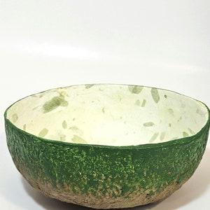 May include: A green and white bowl made of recycled paper. The bowl has a rough, textured exterior and a smooth, white interior.