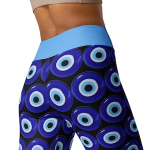May include: Black leggings with a repeating pattern of large blue and white evil eye symbols. The leggings have a light blue waistband and are shown from the waist down. The background is white.