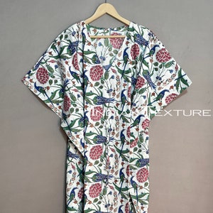 May include: White caftan with a floral and bird pattern in red, blue, and green. The long, flowing garment features a V-neck and wide sleeves. The fabric is printed with a repeating design of stylized birds and flowers.